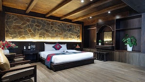 Quarto moderno com parede de destaque em pedra, uma cama grande com almofadas vermelhas e azuis, uma mesa de cabeceira com garrafa e copos, e um vaso de planta.