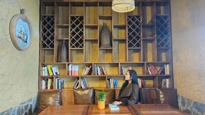 Uma biblioteca com estantes, uma mesa de madeira e uma pessoa sentada.