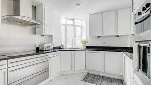 Cocina moderna con armarios blancos, encimera negra, extractor de acero inoxidable y ventana que deja entrar luz natural.