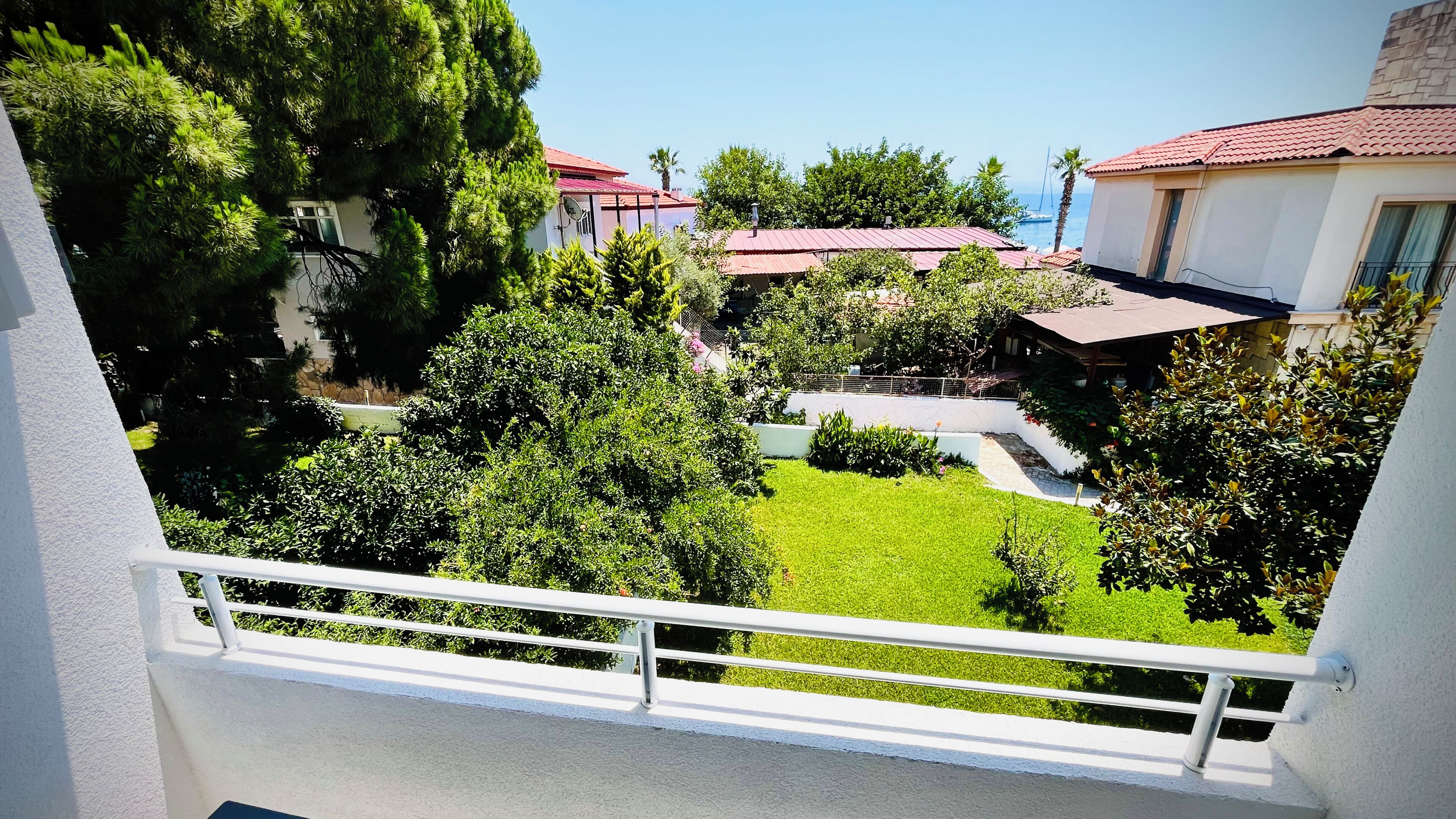 A balcony with a white railing overlooking a well-maintained garden and a view of houses with red roofs.