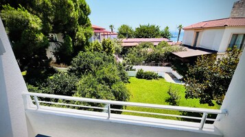 A balcony with a white railing overlooking a well-maintained garden and a view of houses with red roofs.
