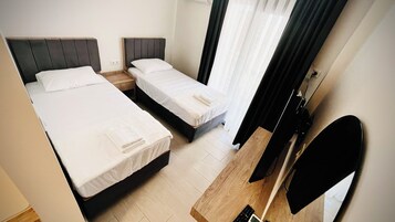 A hotel room with two beds, a wooden nightstand, a TV, and a window with curtains.