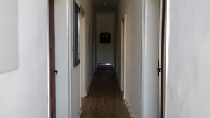 Um corredor estreito com paredes brancas e soalho de madeira, que leva a uma porta no final.