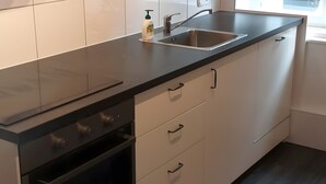 Uma cozinha com bancada preta, pia de aço inoxidável e armários brancos.