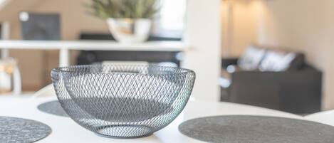 A modern interior with a wire mesh bowl on a white table, a grey sofa, and a plant in the background.