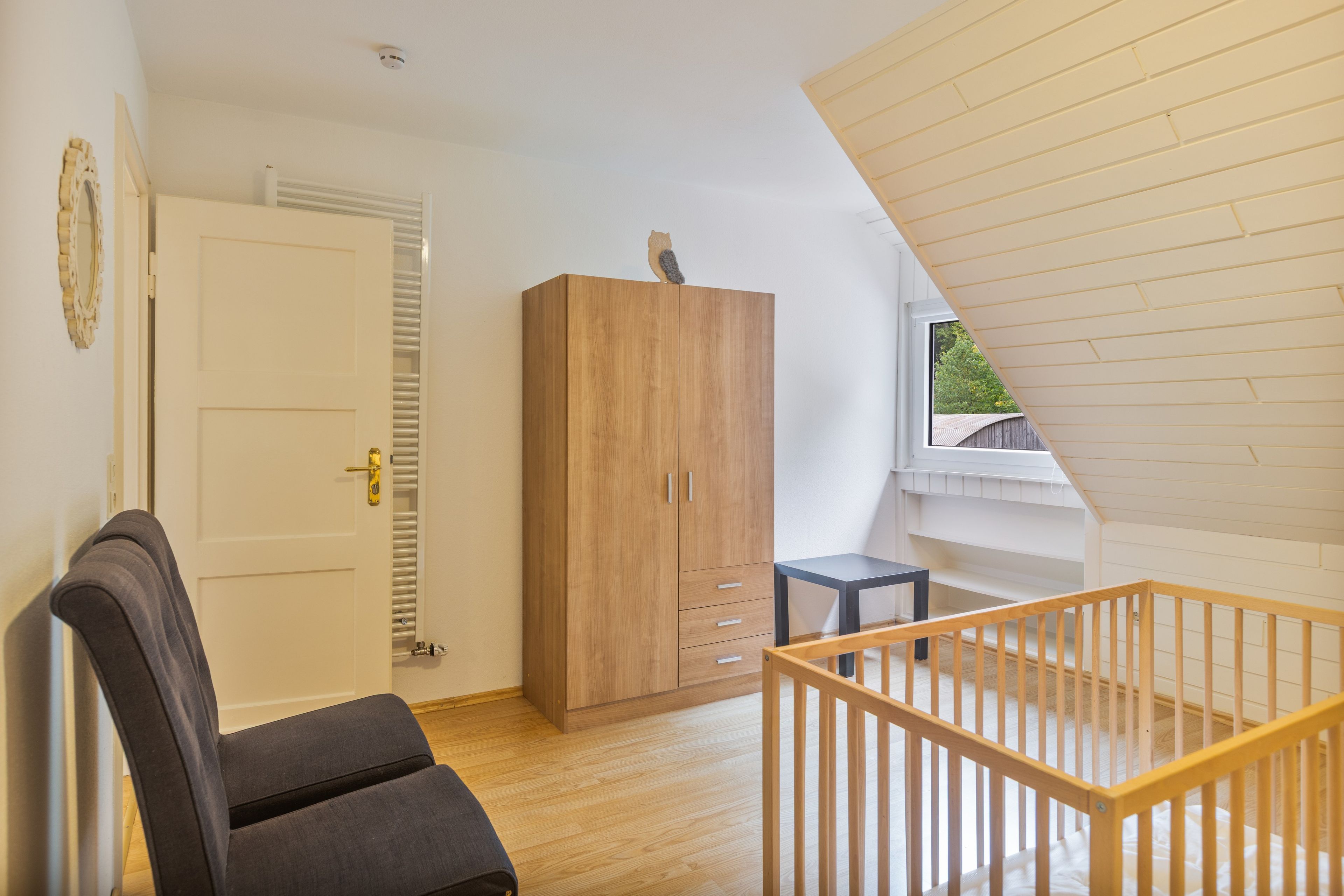 Ein Zimmer mit Holzschrank, einem kleinen Tisch, einem Stuhl und einer Holztreppe.