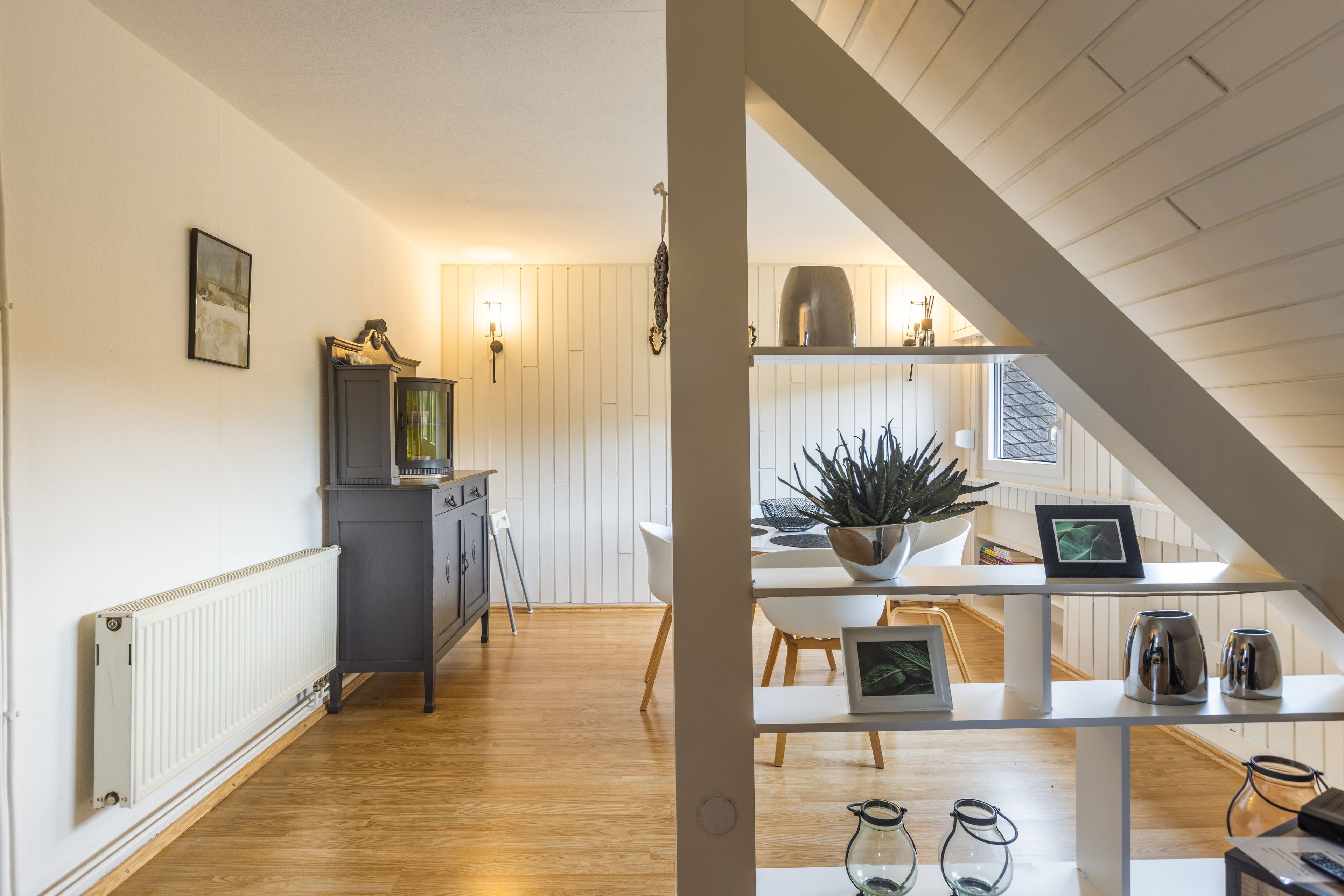 A modern kitchen with wooden flooring, a built-in cabinet, and a hanging light fixture.