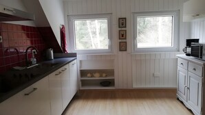Ett kök med vita skåp, en svart bänkskiva, en vattenkokare och en kaffebryggare. Det finns två fönster med utsikt över träd.