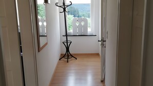 En hall med trägolv, en svart golvlampa, en spegel och ett fönster med utsikt över grönområden.