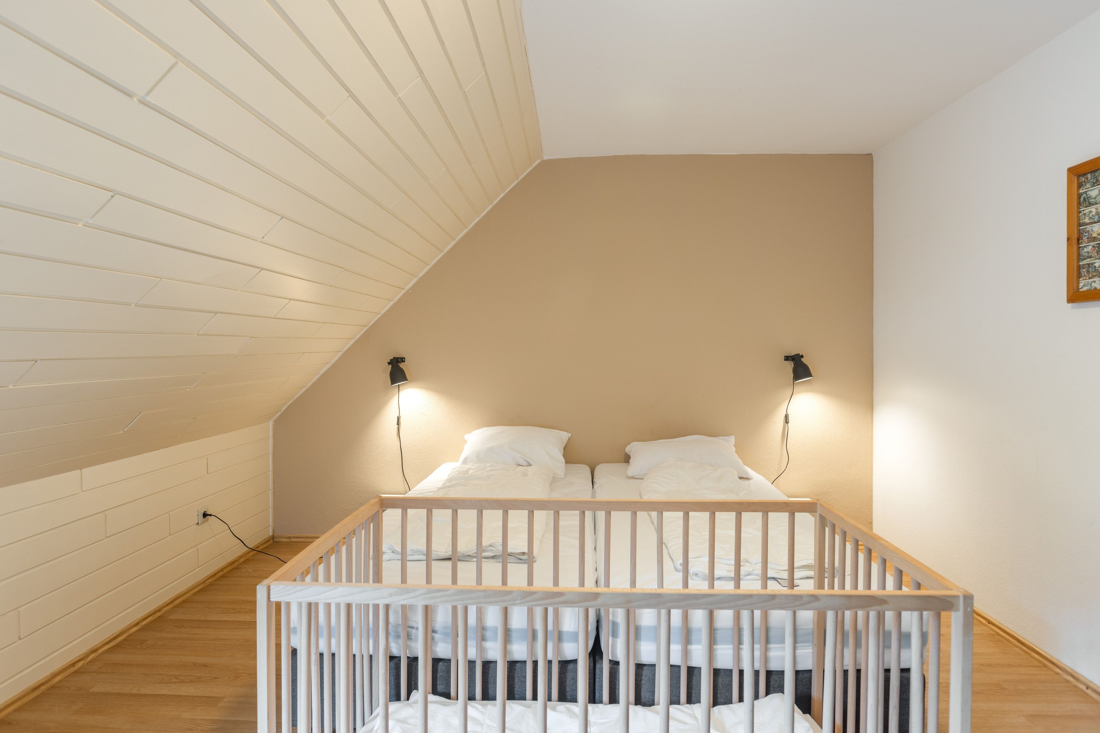Ein Zimmer mit schrägen Wänden, einem Reisebett und zwei Nachttischlampen.