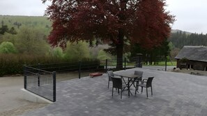 Eine Terrasse im Freien mit Tisch und Stühlen, einem Metallzaun und Blick auf einen bewaldeten Hügel.