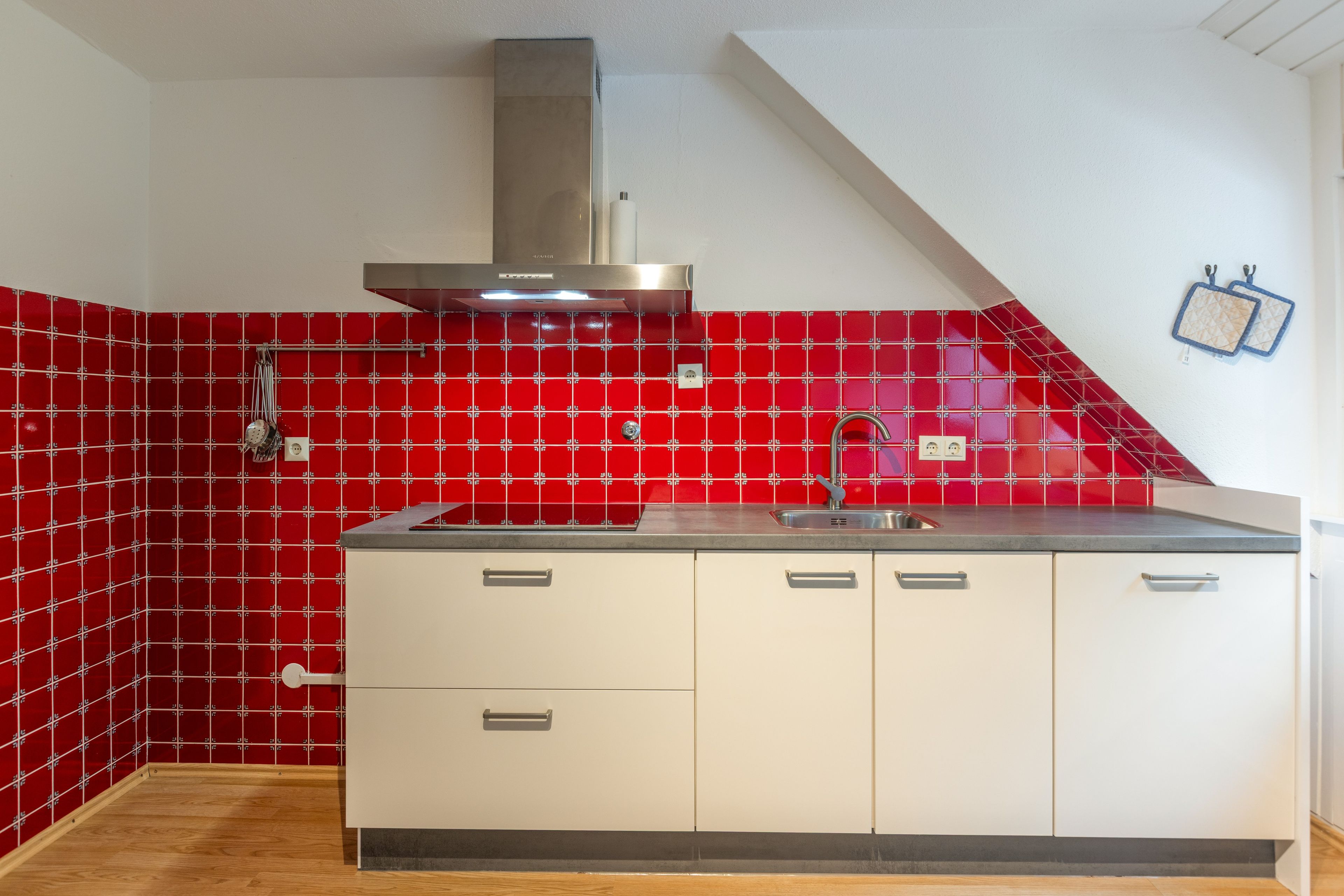 Eine Küche mit roter Fliesenwand, einer Edelstahl-Dunstabzugshaube und einer weißen Arbeitsplatte mit Spüle.