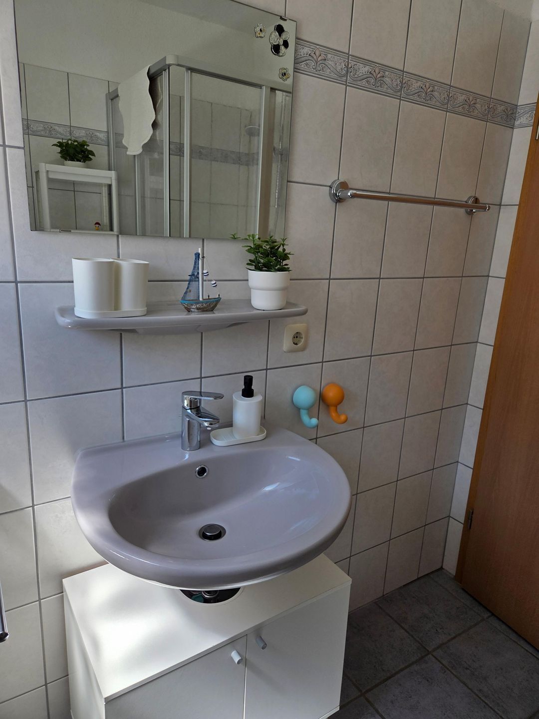 A bathroom with a sink, mirror, towel rack, and a shower enclosure.