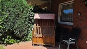 A patio area with a wooden bench, a folding chair, and a small wooden structure. - Vacation Rental at Am Harlebogen 11, Apartment 1 - Vacation Rental at Am Harlebogen 9, Apartment 1 (Wittmund)
