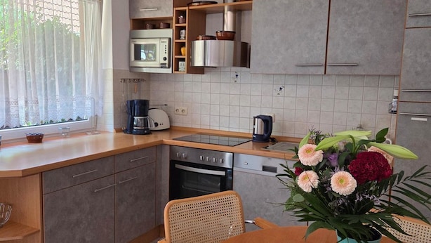 A modern kitchen with a central island, built-in appliances, and a dining area with a vase of flowers. - Vacation Rental at Am Harlebogen 11, Apartment 1 - Vacation Rental at Am Harlebogen 9, Apartment 1 (Wittmund)