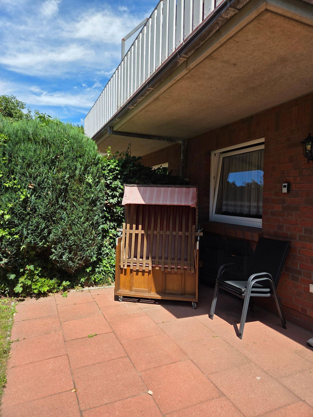 Eine Terrassenfläche mit einer hölzernen Bank, einem Klappstuhl und einer kleinen Holzhütte.