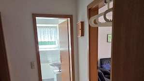A hallway leading to a bathroom with a sink and a window with curtains. - Vacation Rental at Am Harlebogen 11, Apartment 1 - Vacation Rental at Am Harlebogen 9, Apartment 1 (Wittmund)