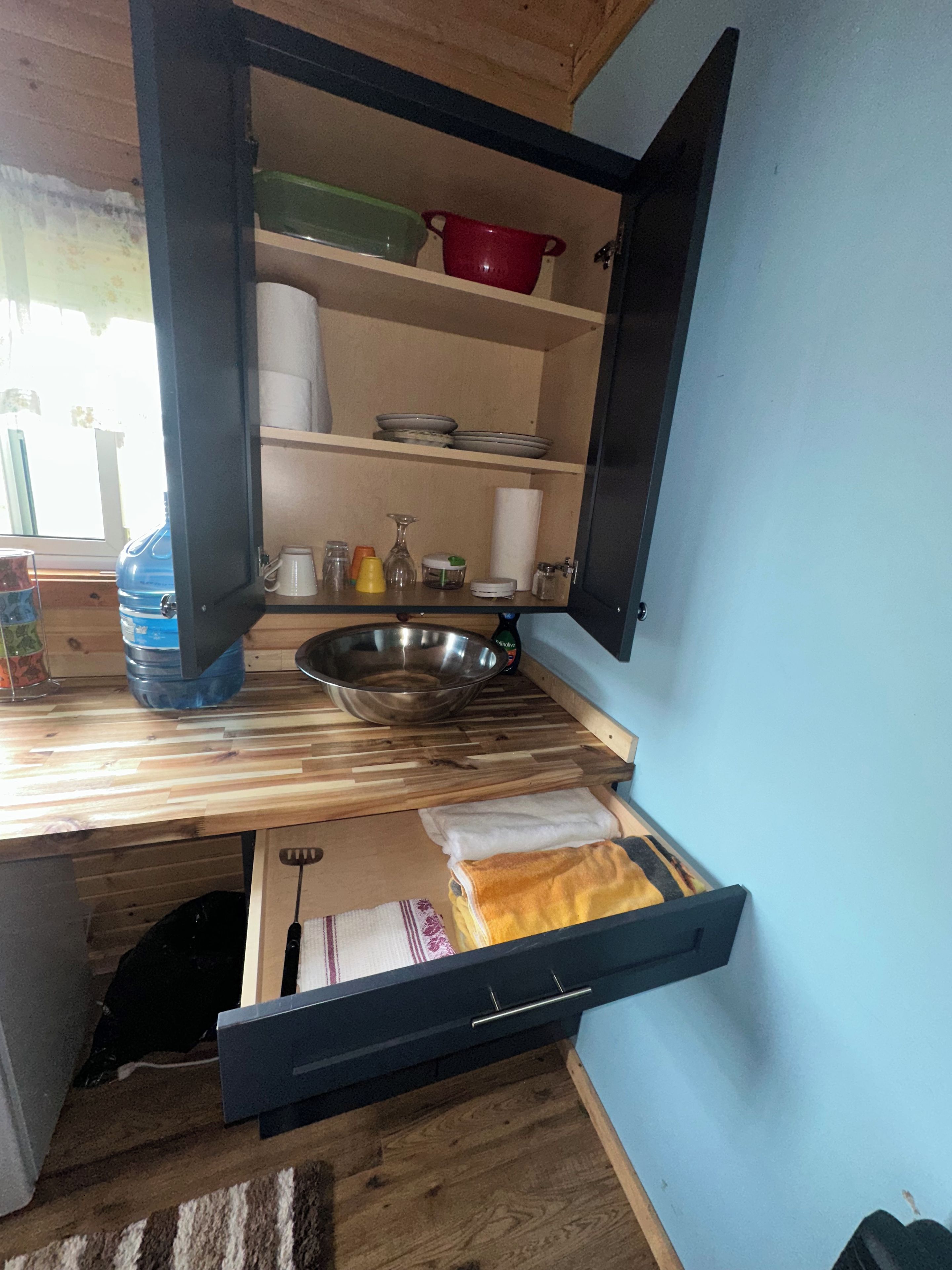 Una cucina compatta con un piano di lavoro in legno, un lavello in acciaio inox e un cassetto integrato.