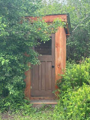 A wooden structure with a door, surrounded by dense greenery.