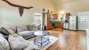 A living room with a sofa, a coffee table, and a kitchen area with cabinets and appliances. - Fire Pit & Yard! Rayburn Country Resort Escape (Brookeland)