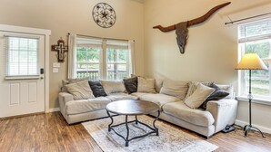 A living room with a sectional sofa, a coffee table, a rug, a wall-mounted cross, and a bull's head decoration. - Fire Pit & Yard! Rayburn Country Resort Escape (Brookeland)