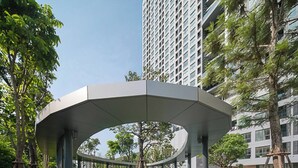 A modern architectural structure with a curved roof, surrounded by greenery and adjacent to a high-rise building. - Ideo O2 condo style resort BTS Bangna (Bangkok)