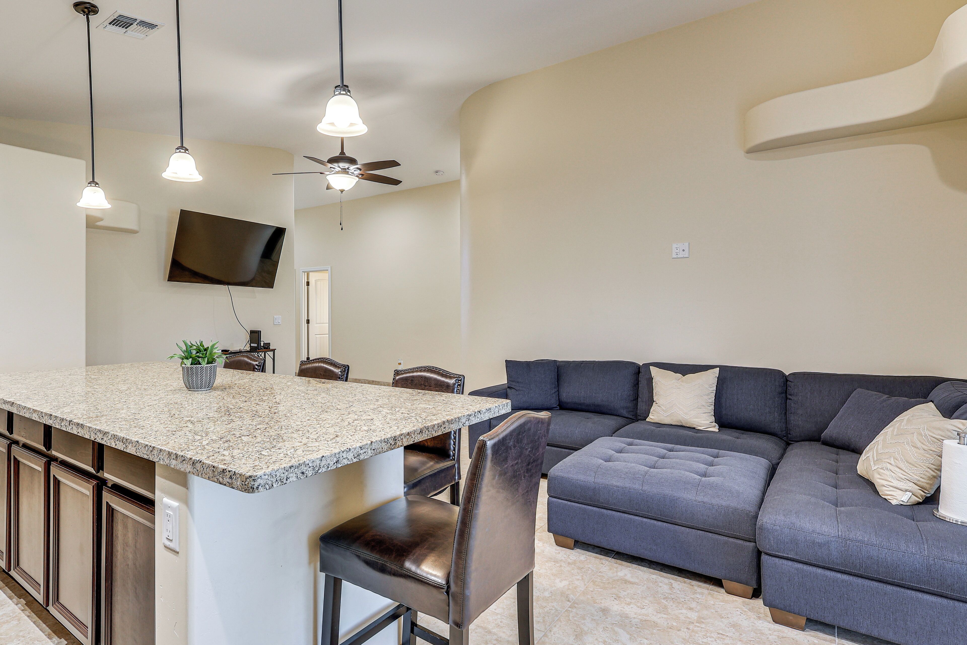 A modern kitchen with granite countertops, a dining area with a dark-colored sofa, and a ceiling fan.