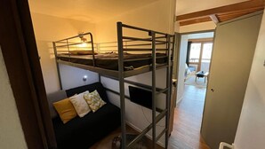 Un letto a castello con una scrivania e un divano in una stanza con una porta che dà su un'altra area.