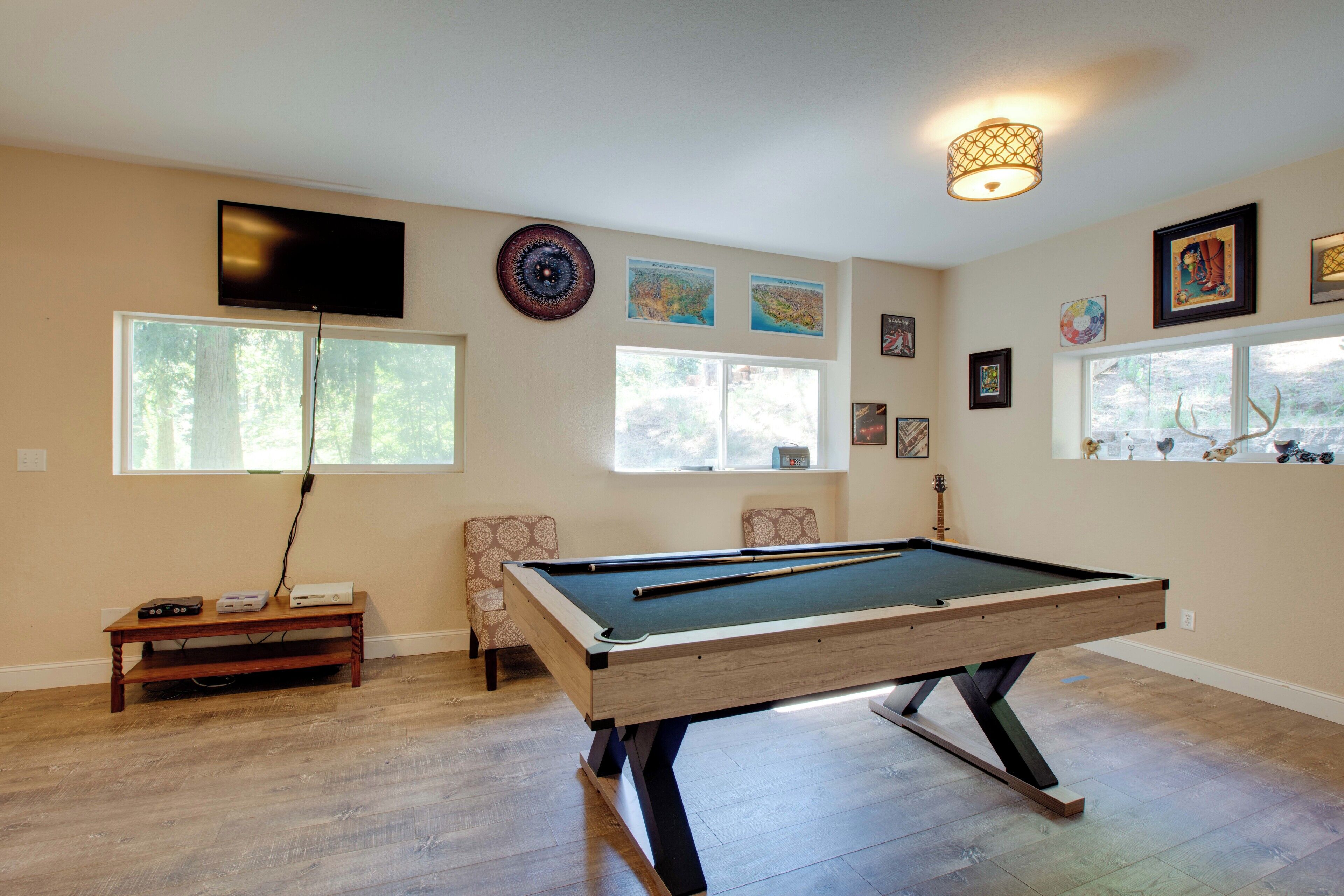 A pool table in a room with a television, artwork, and a window with a view of trees.