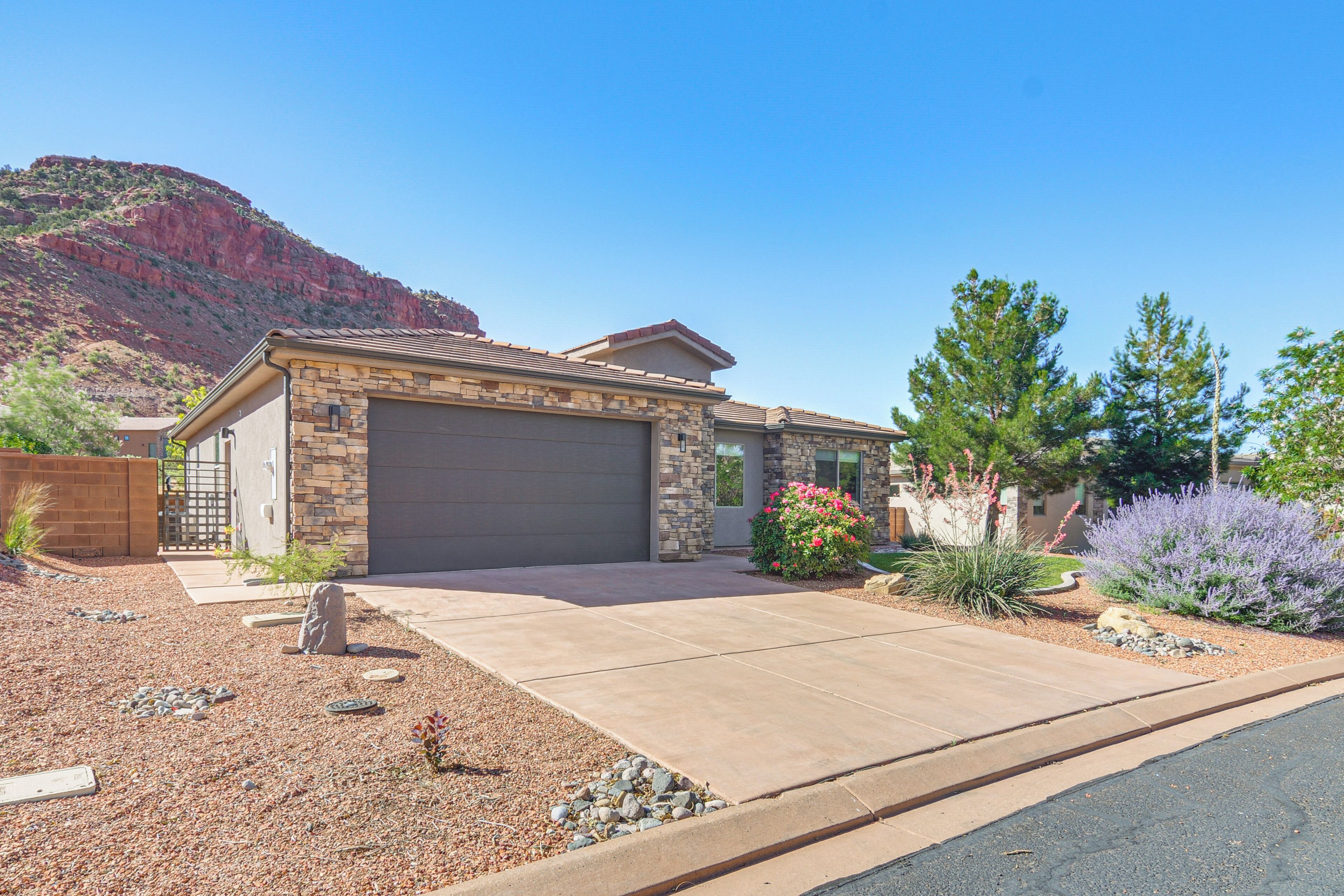 A single-story house with a garage, surrounded by a landscaped garden with various plants and a mountain in the background.