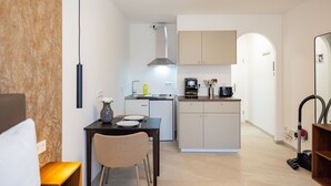 A compact kitchen with a dining area, a coffee machine, and a vacuum cleaner. - Charming Studio for a Relaxing Würzburg Stay (Würzburg)