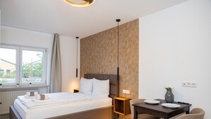 A modern bedroom with a bed, bedside table, and a small dining area with chairs and a table. - Charming Studio for a Relaxing Würzburg Stay (Würzburg)