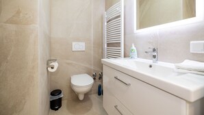 A bathroom with a toilet, a sink, a mirror, and a towel rack. - Charming Studio for a Relaxing Würzburg Stay (Würzburg)
