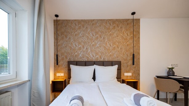 A hotel room with a bed, two bedside tables, a desk, a chair, and a window. - Charming Studio for a Relaxing Würzburg Stay (Würzburg)