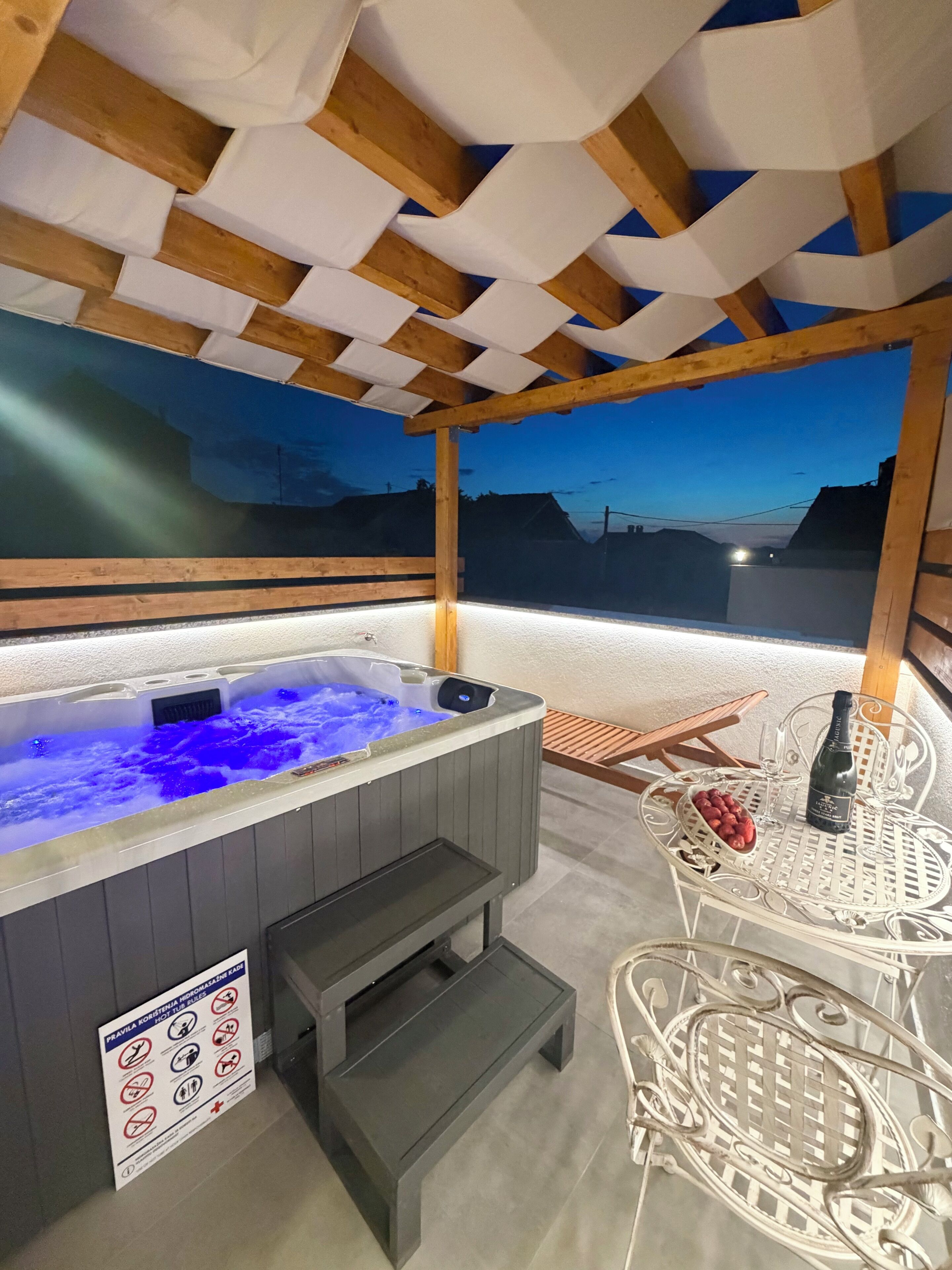 A hot tub with a wooden ceiling, a table with a bottle and fruit, and a sign with rules.