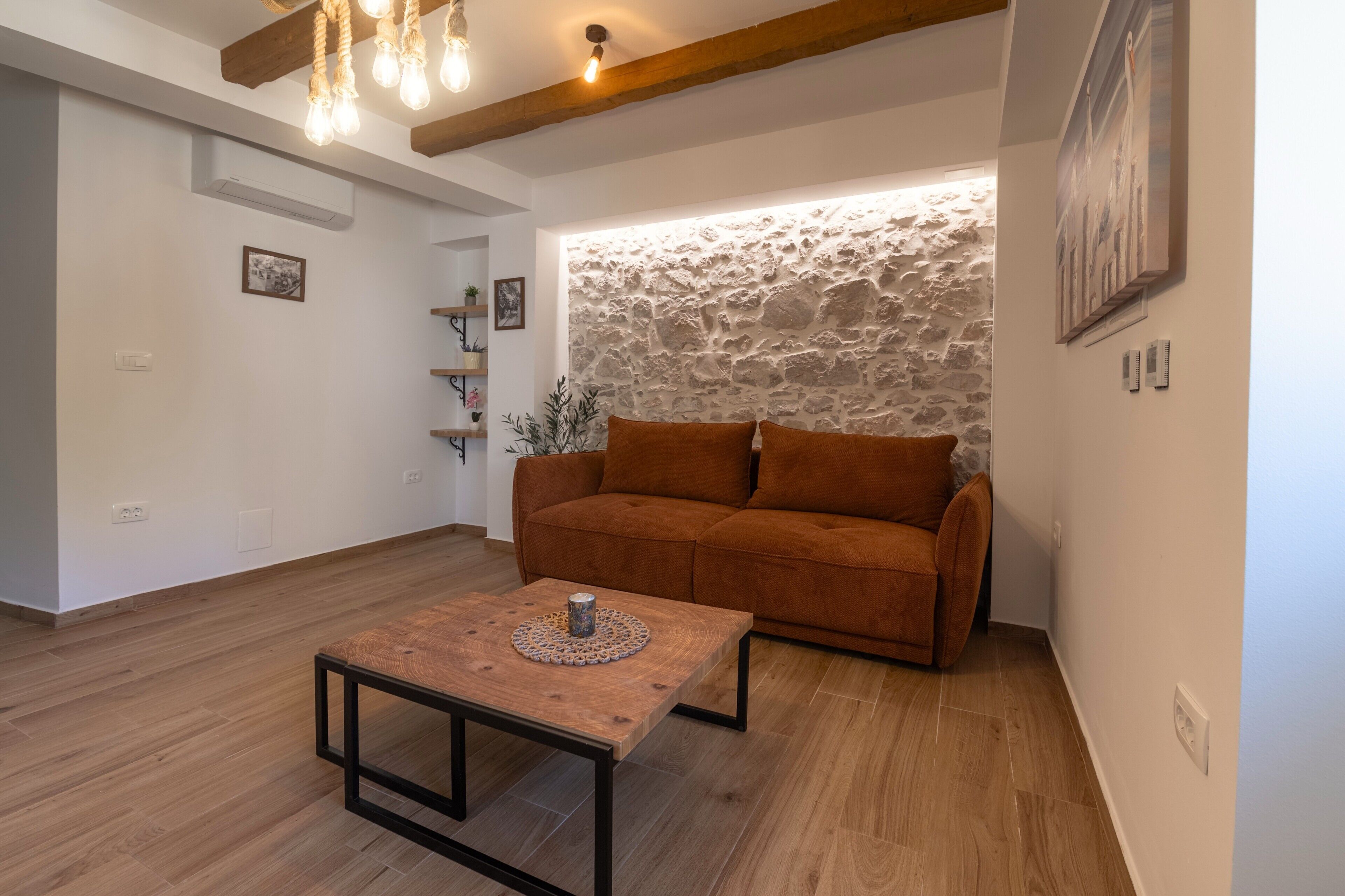 A living room with a brown sofa, a wooden coffee table, and a stone wall.