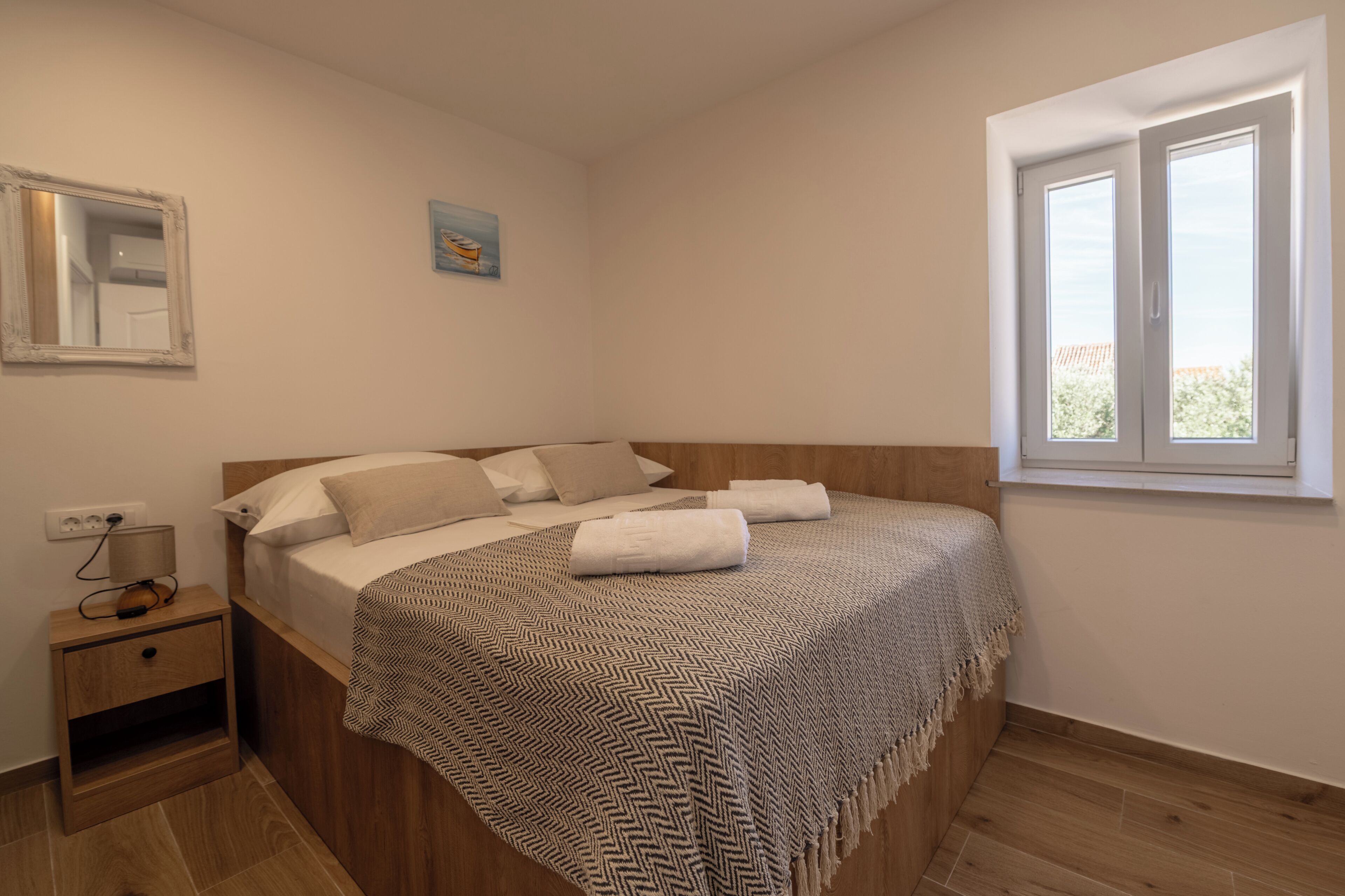 Ein Schlafzimmer mit einem Bett, einem Nachttisch, einer Lampe, einem Gemälde und einem Fenster.