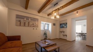 A living room with a wooden floor, a sofa, a coffee table, a painting, a window, and a dining area in the background. - Blažov Dvor (Zaton)