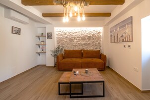 A living room with a sofa, a coffee table, a stone wall, and a painting of birds.