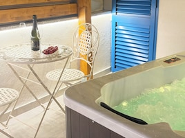 A hot tub, a table with a bottle and glasses, and a chair.