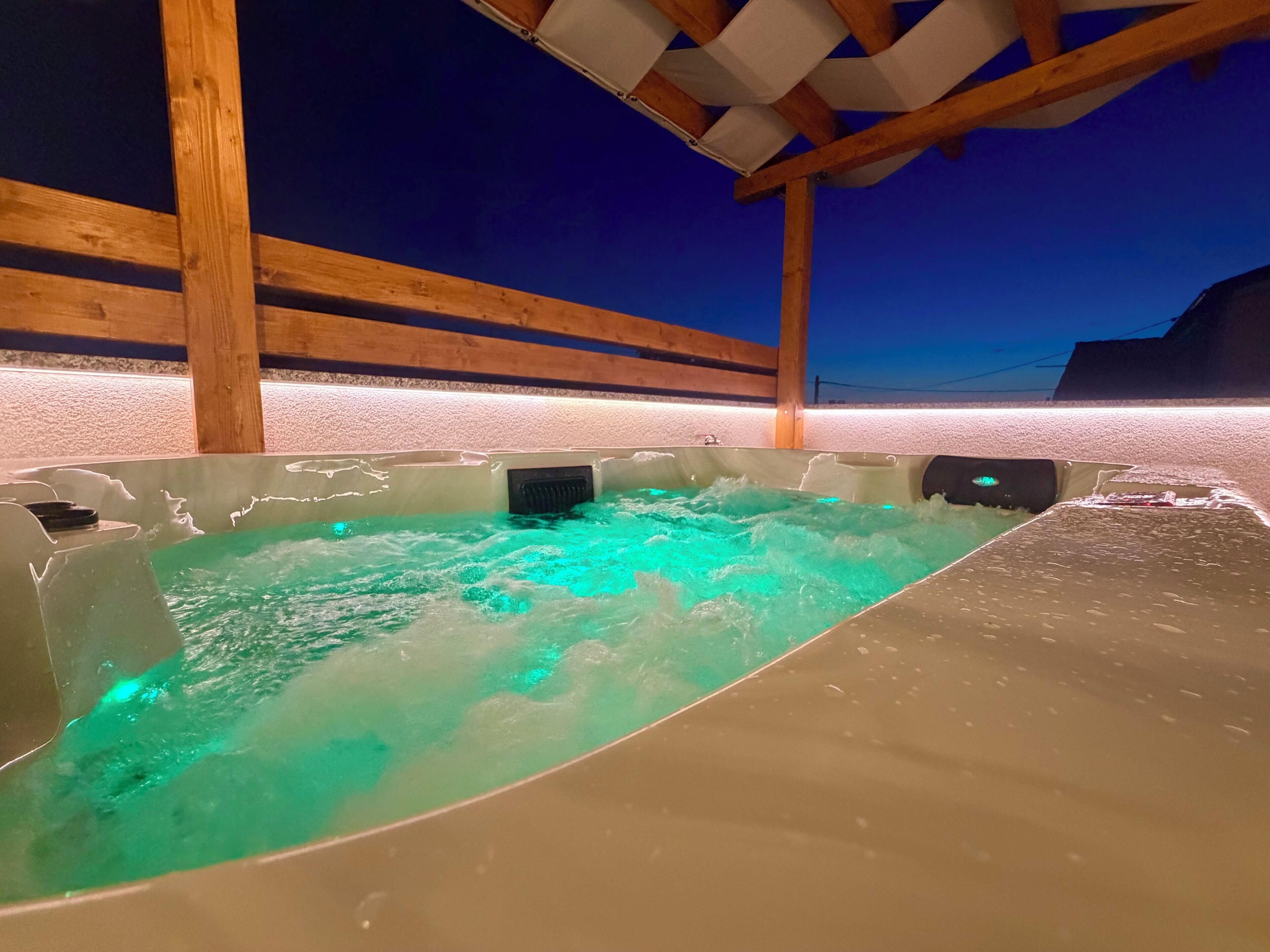 A hot tub with a wooden structure overhead, surrounded by a sandy area.