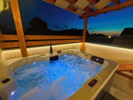 A hot tub with a control panel, a bottle, and glasses on the edge.