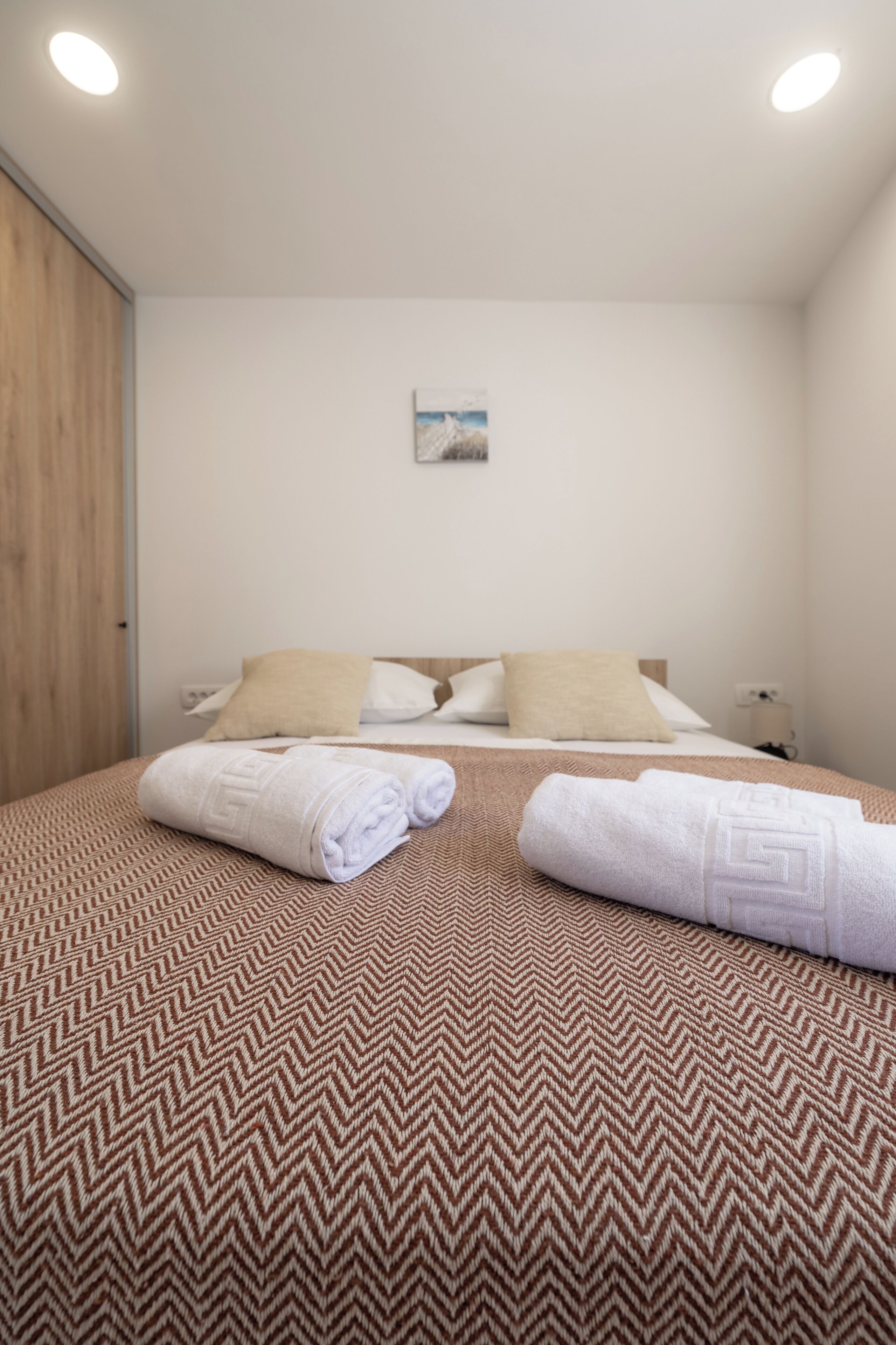 A hotel room with a bed, two pillows, a nightstand, a lamp, and a painting on the wall.