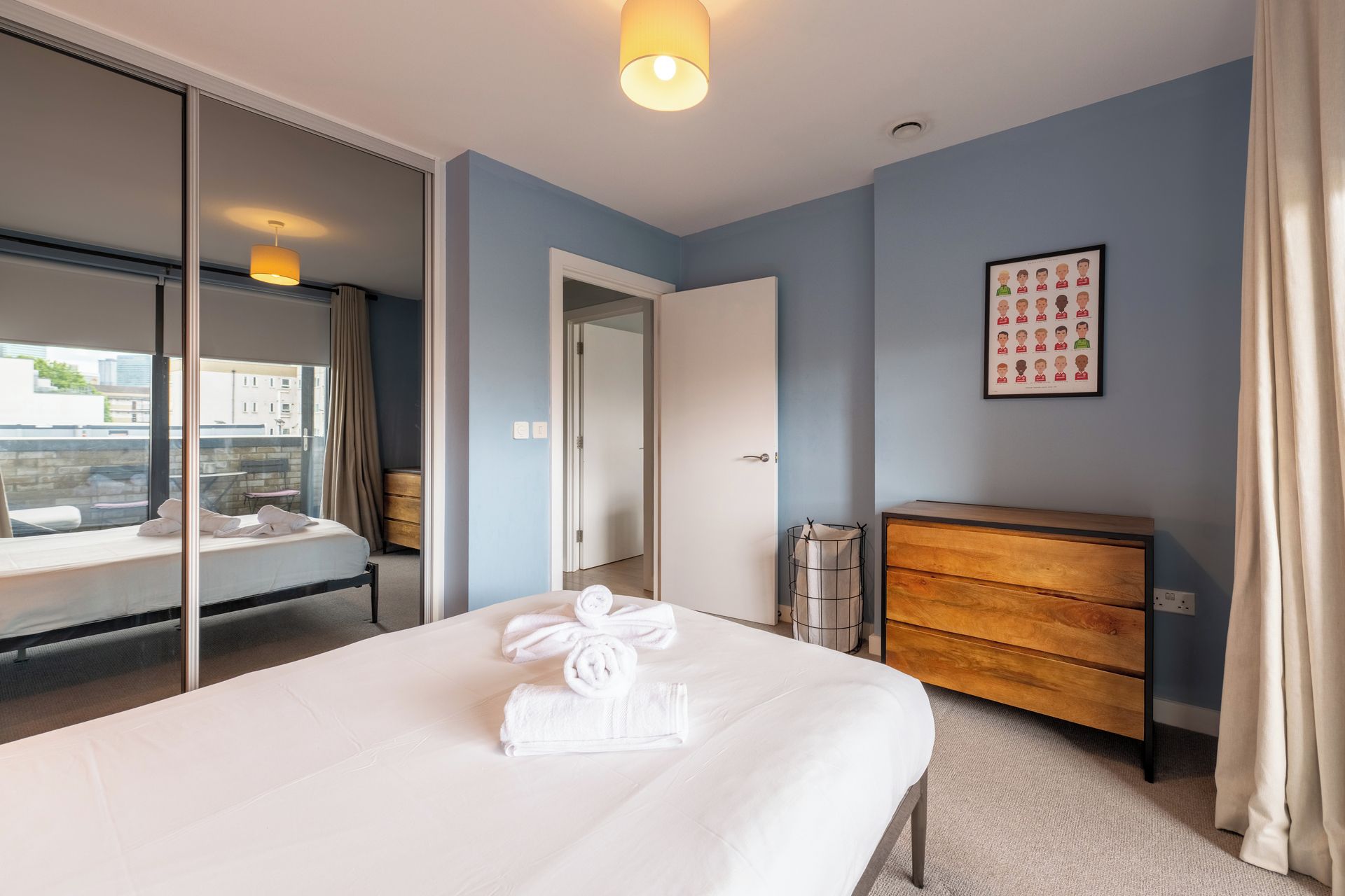 A hotel room with a bed, a dresser, a mirror, a framed picture on the wall, and a window with a view of buildings.
