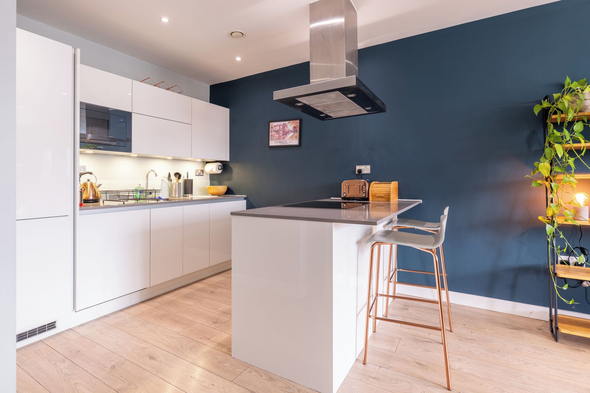 Una cocina moderna con armarios blancos, una campana extractora de acero inoxidable y una isla de madera con taburetes de bar.