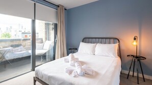 A hotel room with a bed, a view of the city, and a balcony with outdoor furniture. - Contemporary East London Hideaway with Balcony (Greater London)