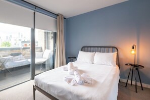 A hotel room with a bed, a view of the city, and a balcony with outdoor furniture. - Contemporary East London Hideaway with Balcony (Greater London)