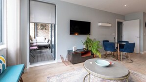 A modern living room with a flat-screen TV, a dining area with blue chairs, a sofa, and a coffee table. - Contemporary East London Hideaway with Balcony (Greater London)