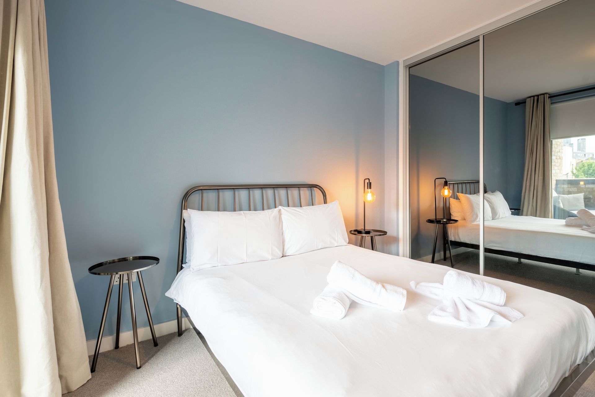 Een hotelkamer met een bed, twee nachtkastjes, een spiegel en uitzicht op buiten.