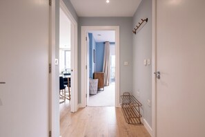 A hallway with a wooden floor, a metal rack, and a door leading to a room with a blue wall and a window. - Contemporary East London Hideaway with Balcony (Greater London)